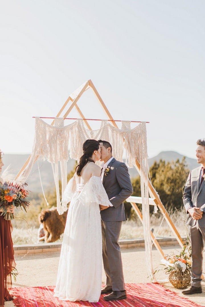 Newlyweds kissing beneath a geometric ceremony arch